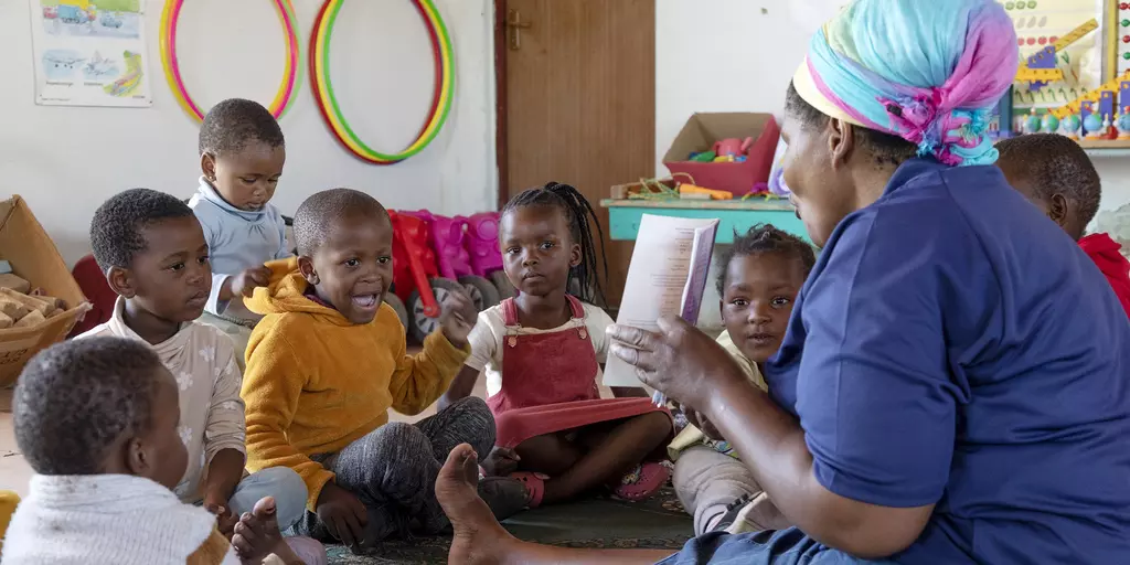 Eine Erzieherin in einer Kita in Südafrika liest mit den Kindern ein Buch.