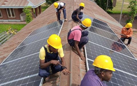 Solar technicians in training install solar panels on a roof.