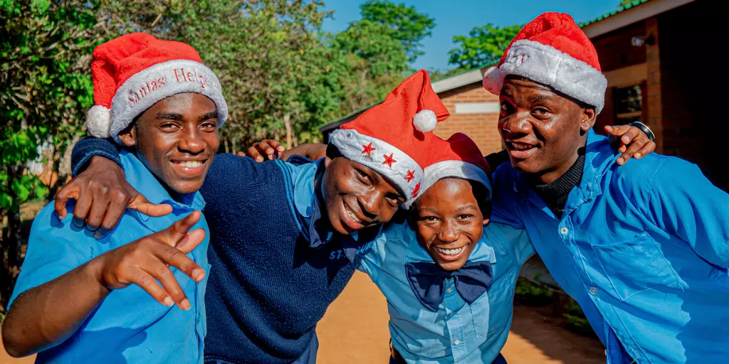 Vier Jugendliche mit Weihnachtsmützen grüßen von der St. Mauritius-Sekundarschule.