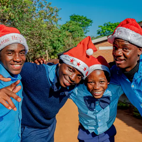 Vier Jugendliche mit Weihnachtsmützen grüßen von der St. Mauritius-Sekundarschule.